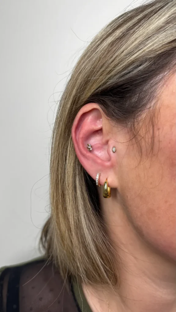 Oreille droite d'une femme avec plusieurs piercings et des bijoux dorés, dont des créoles et un petit stud serti de diamants.