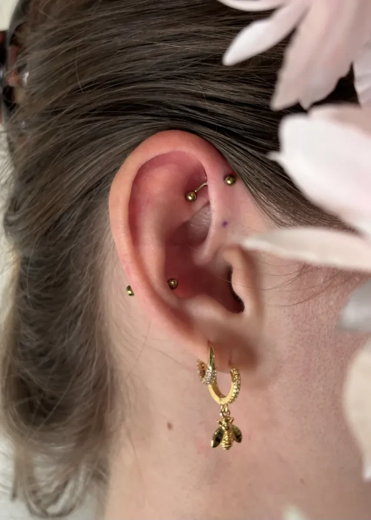 Gros plan sur une oreille avec plusieurs piercings, dont un industriel, un tragus et un lobe, ornée d'une boucle d'oreille en forme d'abeille dorée.