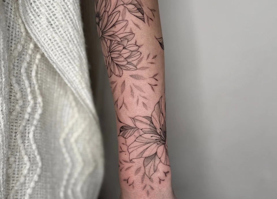 Gros plan d'un tatouage de style fineline représentant des fleurs et des feuilles sur un avant-bras.
