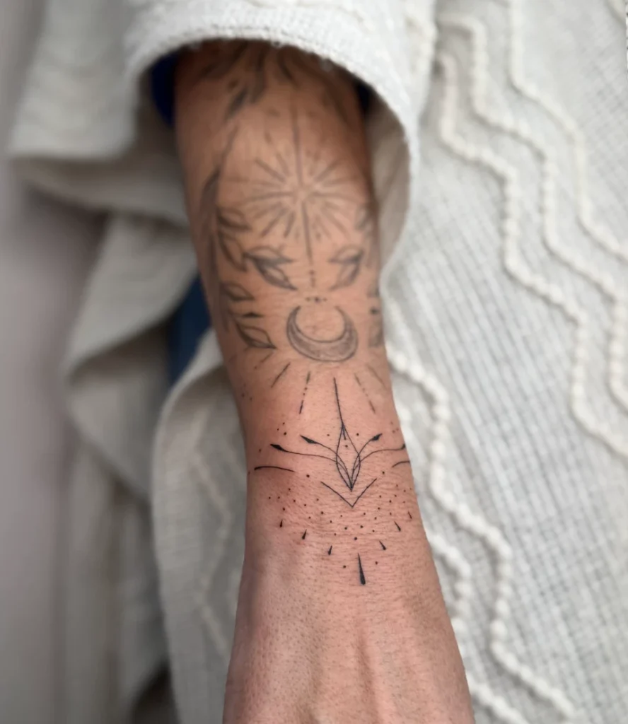 Tatouage minimaliste au poignet représentant une lune croissante, des rayons de soleil et une étoile stylisée.