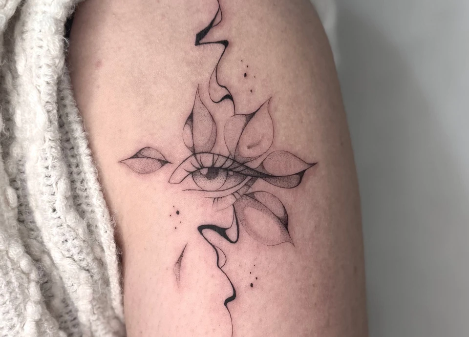 Tatouage réaliste d'un œil entouré de pétales stylisés, évoquant une fleur épanouie avec des lignes fines et quelques points dispersés.