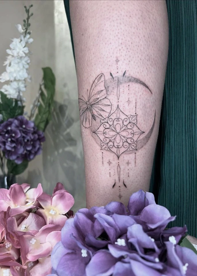Tatouage d'un papillon, d'un croissant de lune et d'un motif floral complexe sur une jambe.