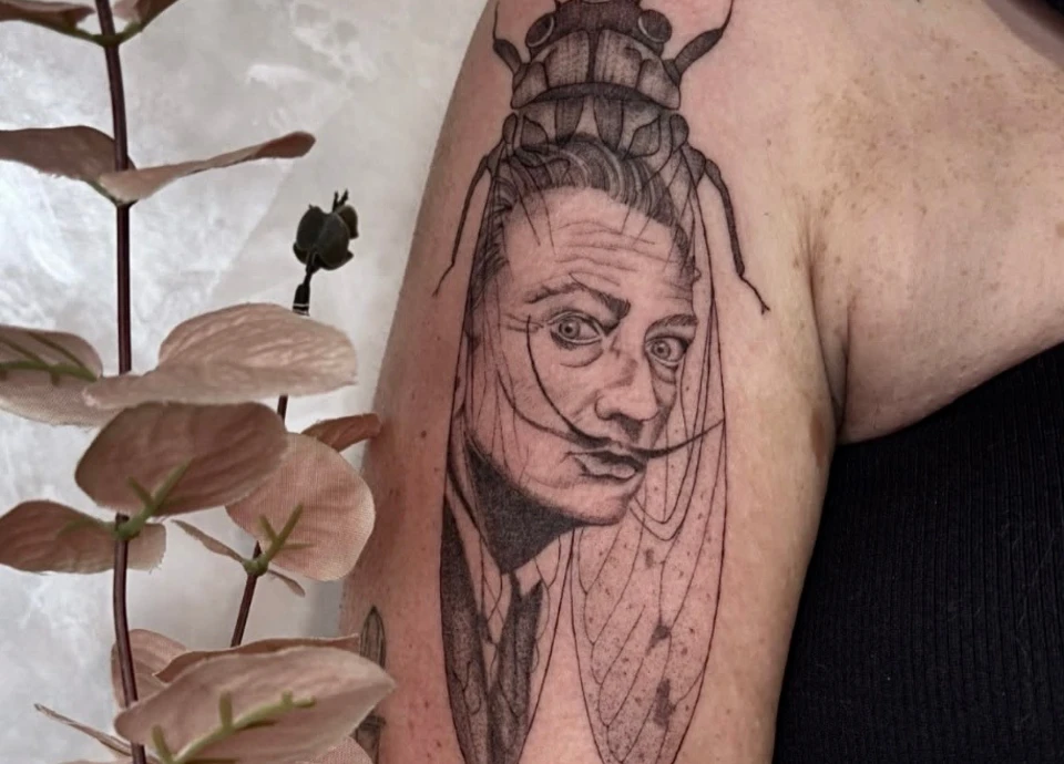 Tatouage représentant le visage de Salvador Dalí fusionné avec une cigale, sur un bras.